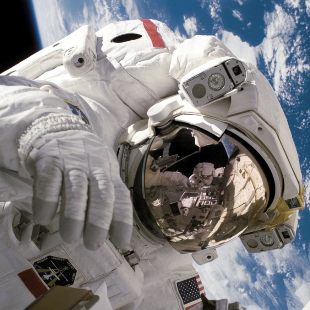 A man who wears a space suit is taking a selfie with the Earth