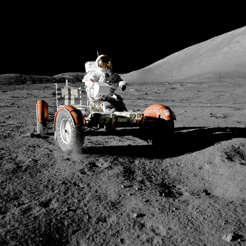 A man who wears a space suit is driving a small car on the Moon